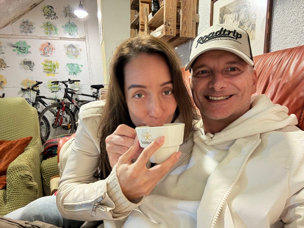 Mosolygó pár közös szelfin, egyikük kávéscsészét tart