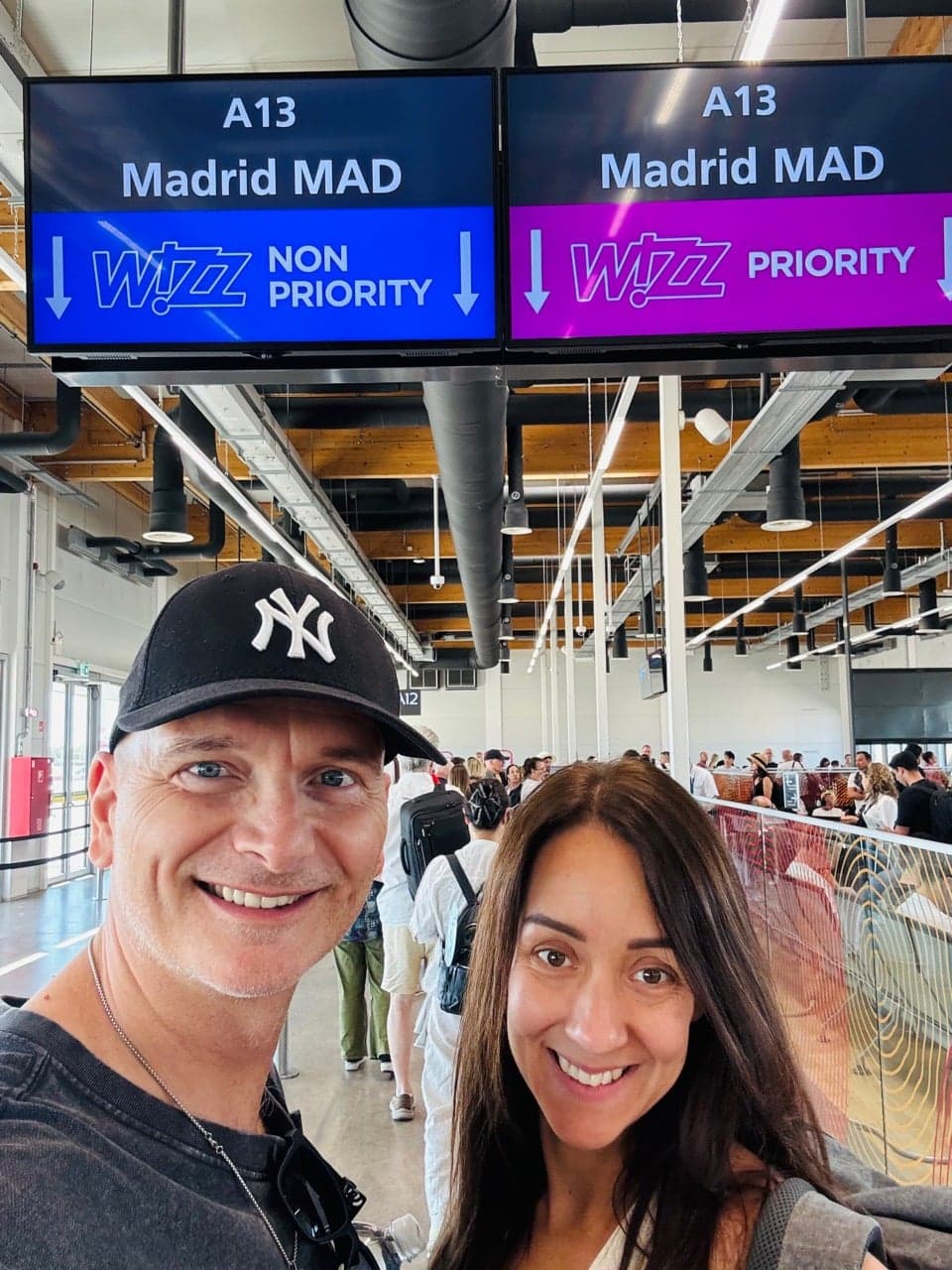 Két utazó szelfije a Madrid feliratú repülőtéri beszállókapu előtt